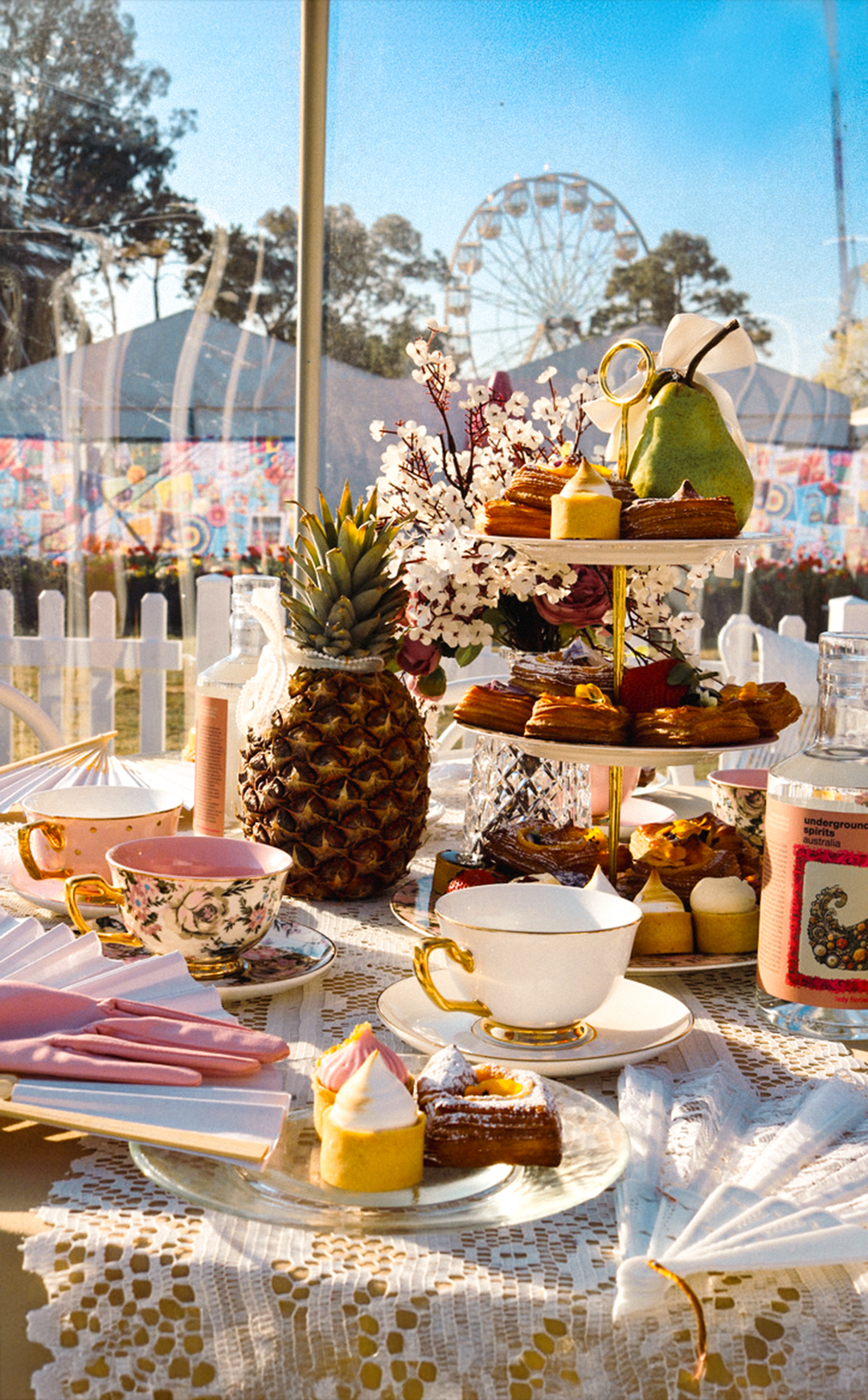 Underground Spirits High Tea setup with pastries, teacups, and a tiered cake stand outdoors at Floriade. Collectors and Explorers Gin