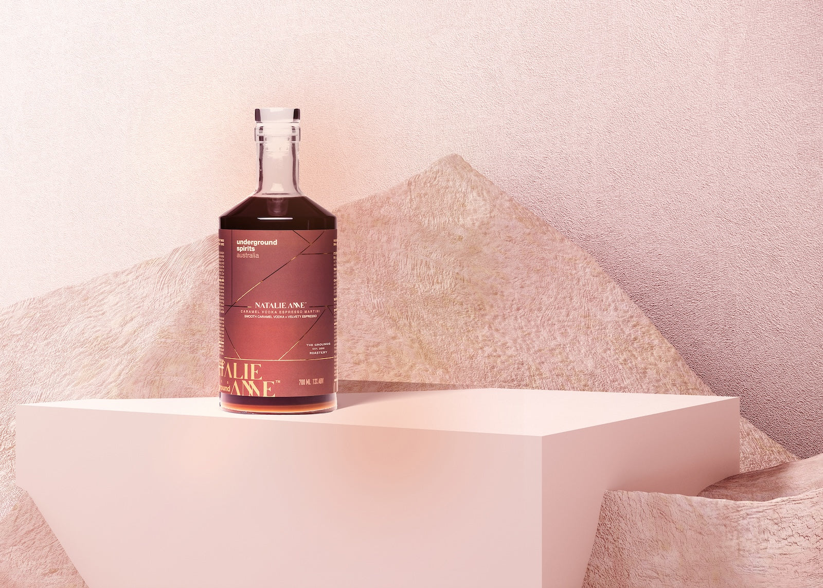 Underground Spirits Australia x Natalie Anne Limited Edition Caramel Espresso Martini sits elegantly on a minimalist pedestal, surrounded by abstract textures and pink lighting
