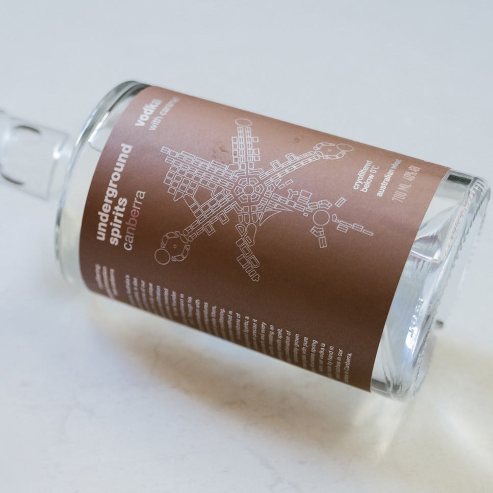 Photo of a sleek, transparent caramel vodka bottle featuring an elegant map of canberra. The bottle is filled with vodka, reflecting light to showcase its premium quality. Positioned against a soft, neutral background to emphasise the luxurious appearance.